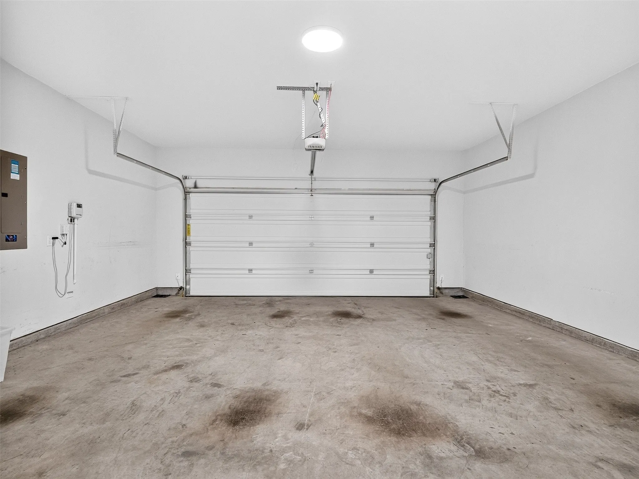 Spacious two-car garage featuring a white overhead door, concrete flooring, and a ceiling-mounted light fixture