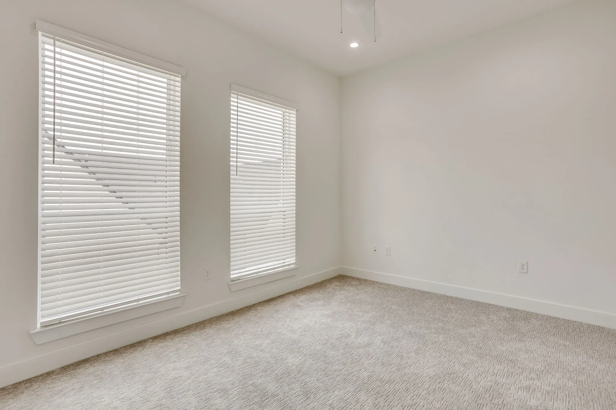 Bright interior space featuring two windows with horizontal blinds, carpeted flooring, white walls, and a recessed ceiling light