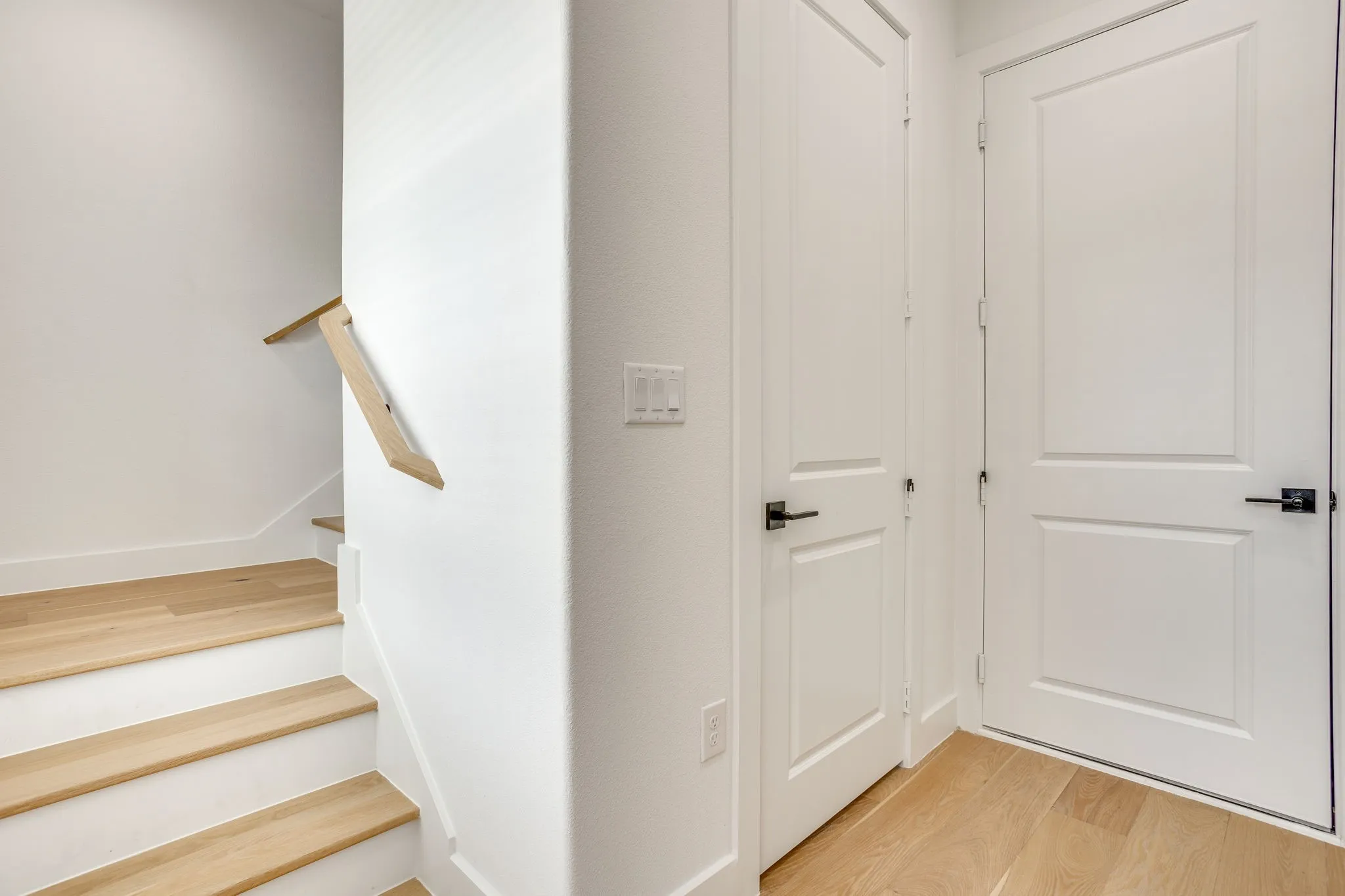 Light wood-finish flooring extending into the staircase featuring white risers and a natural wood handrail
