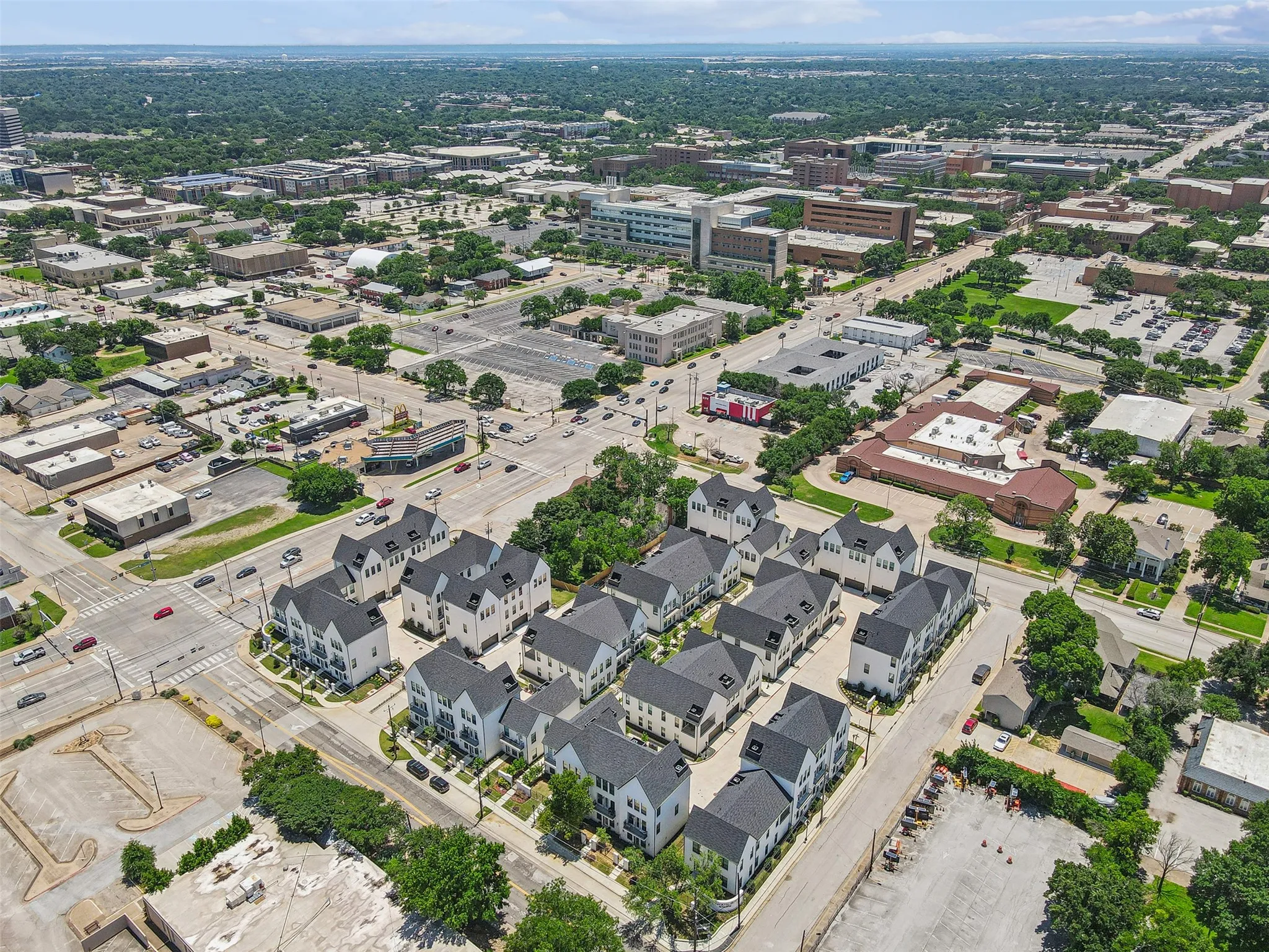 Aerial perspective showcasing a collection of residential townhomes with dark roofs and light-colored exteriors, situated within an urban environment