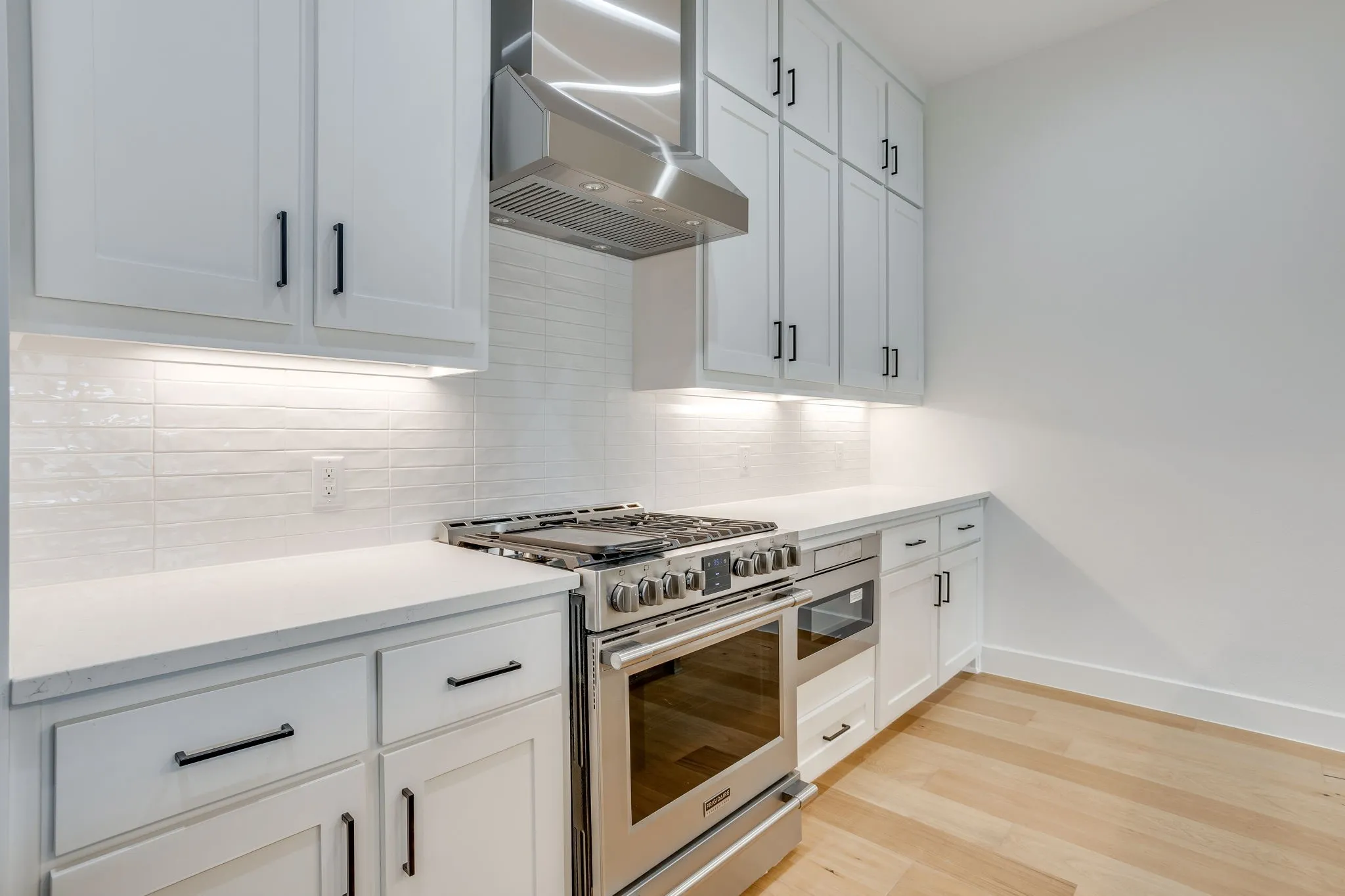 Modern kitchen featuring white shaker cabinetry, stainless steel range with matching hood, quartz countertops, and a white subway tile backsplash