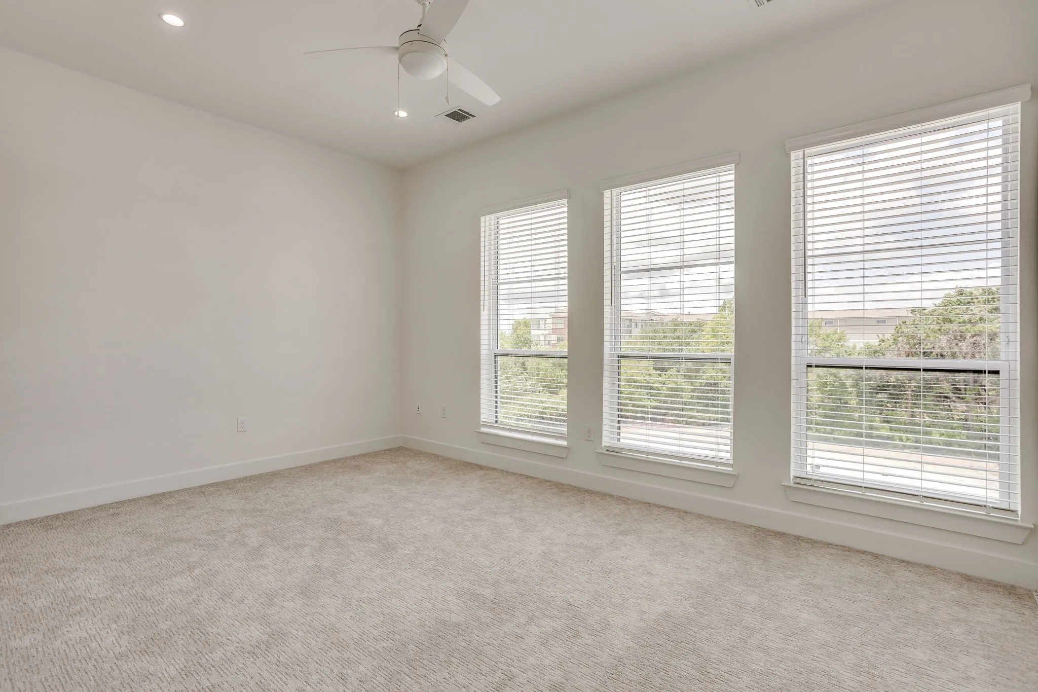 Carpeted room featuring three vertical windows with blinds, a white ceiling fan, and recessed lighting