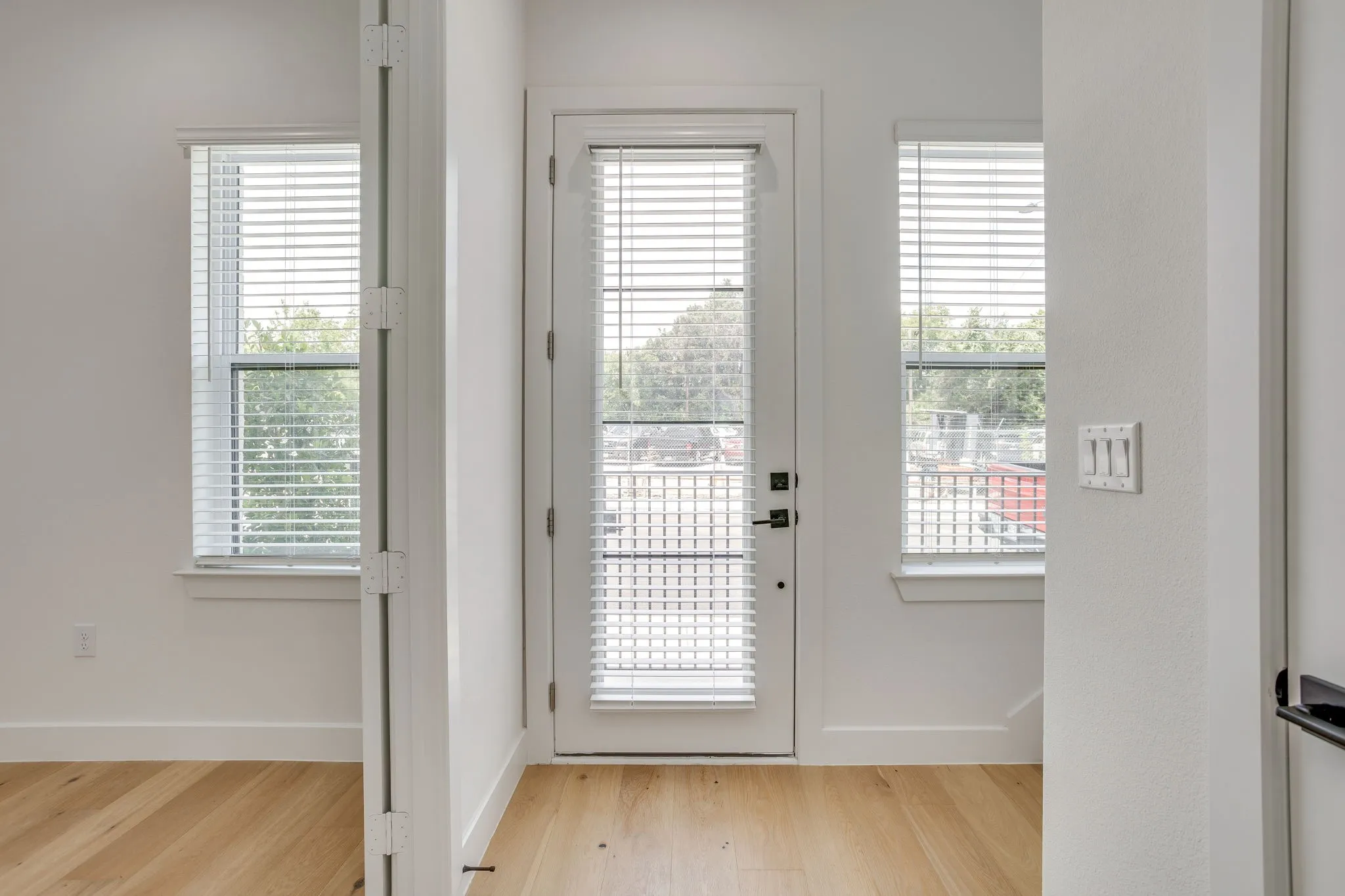 Interior space featuring wood-finish flooring, white walls, and a glass-paneled door with integrated blinds