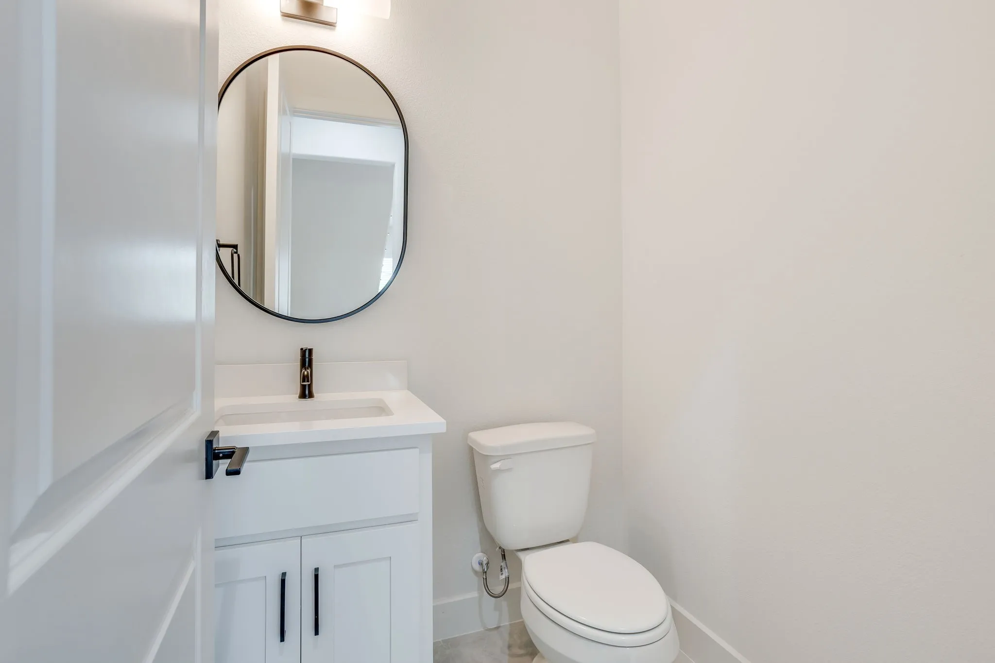 White vanity with integrated sink, black faucet, and oval mirror