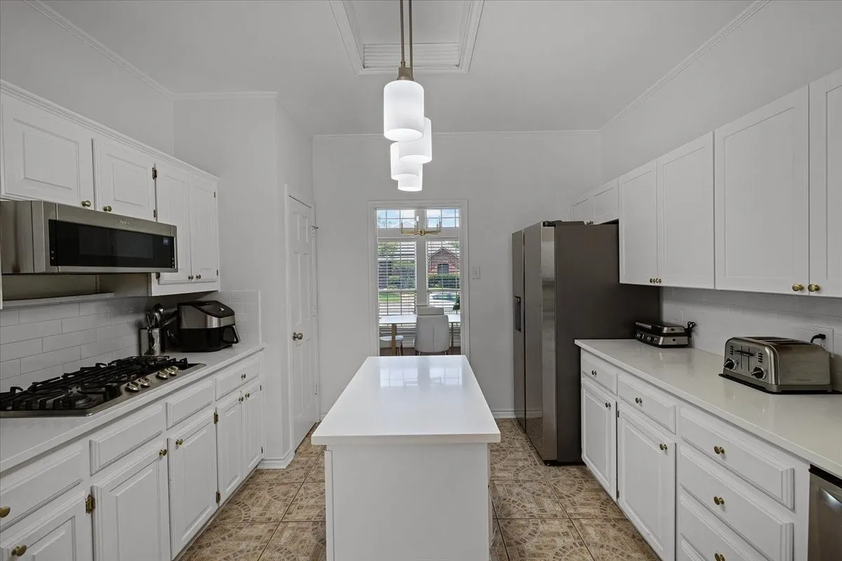 Galley kitchen featuring white cabinetry, a white countertop island, a gas range, a built-in stainless steel microwave, and tile flooring