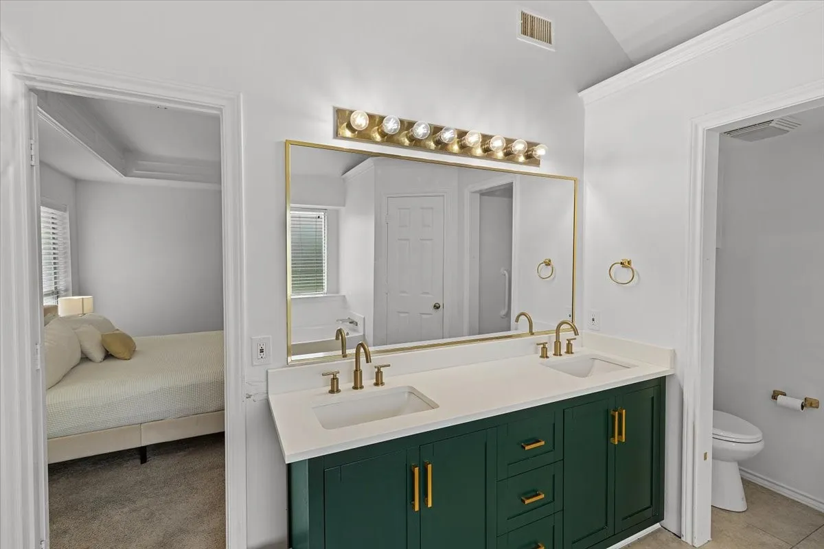 Primary Bathroom - Dual vanity featuring a dark green cabinet with gold hardware, white countertop, and gold-finish faucets