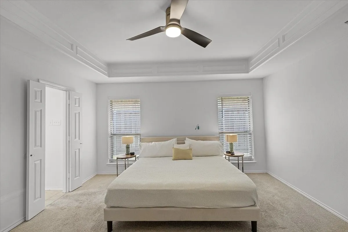 Primary Bedroom - Tray ceiling with crown molding, ceiling fan, carpeting, two windows with blinds, and white panel doors