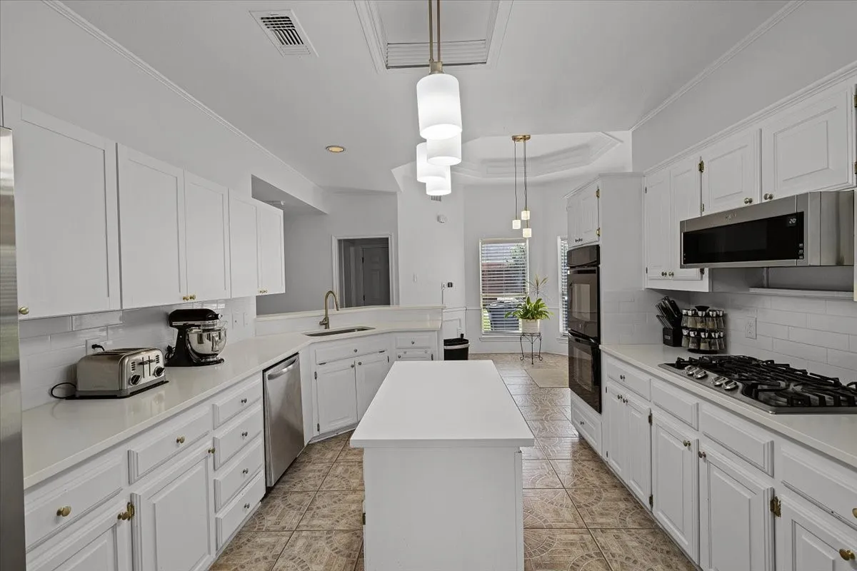 Kitchen featuring a central island, white cabinetry, integrated stainless steel appliances, and tile flooring