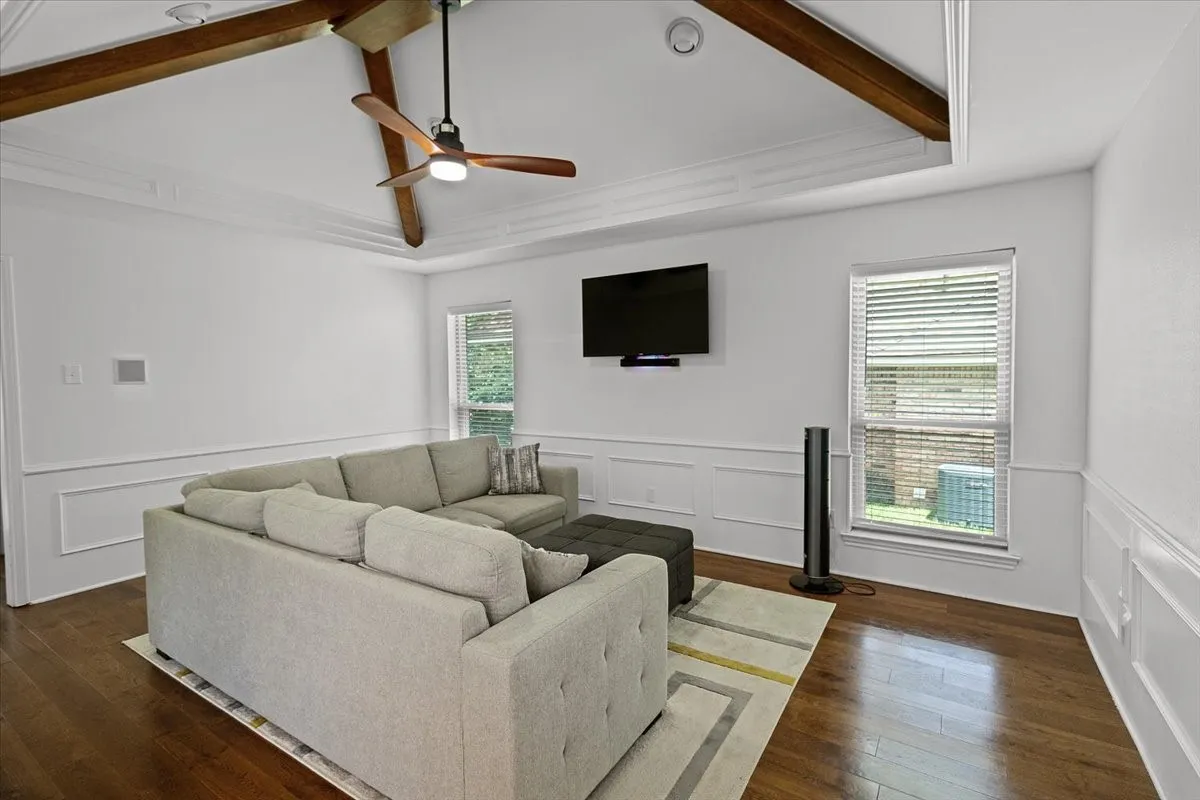 Family Room -Spacious room featuring wood-finish flooring, white paneled wainscoting, and a white tray ceiling with exposed wood beams