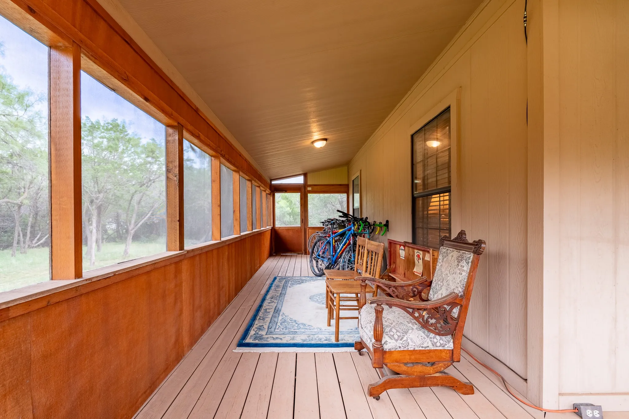 Expansive screened porch featuring wood-finish flooring, wood-paneled walls, and multiple overhead light fixtures