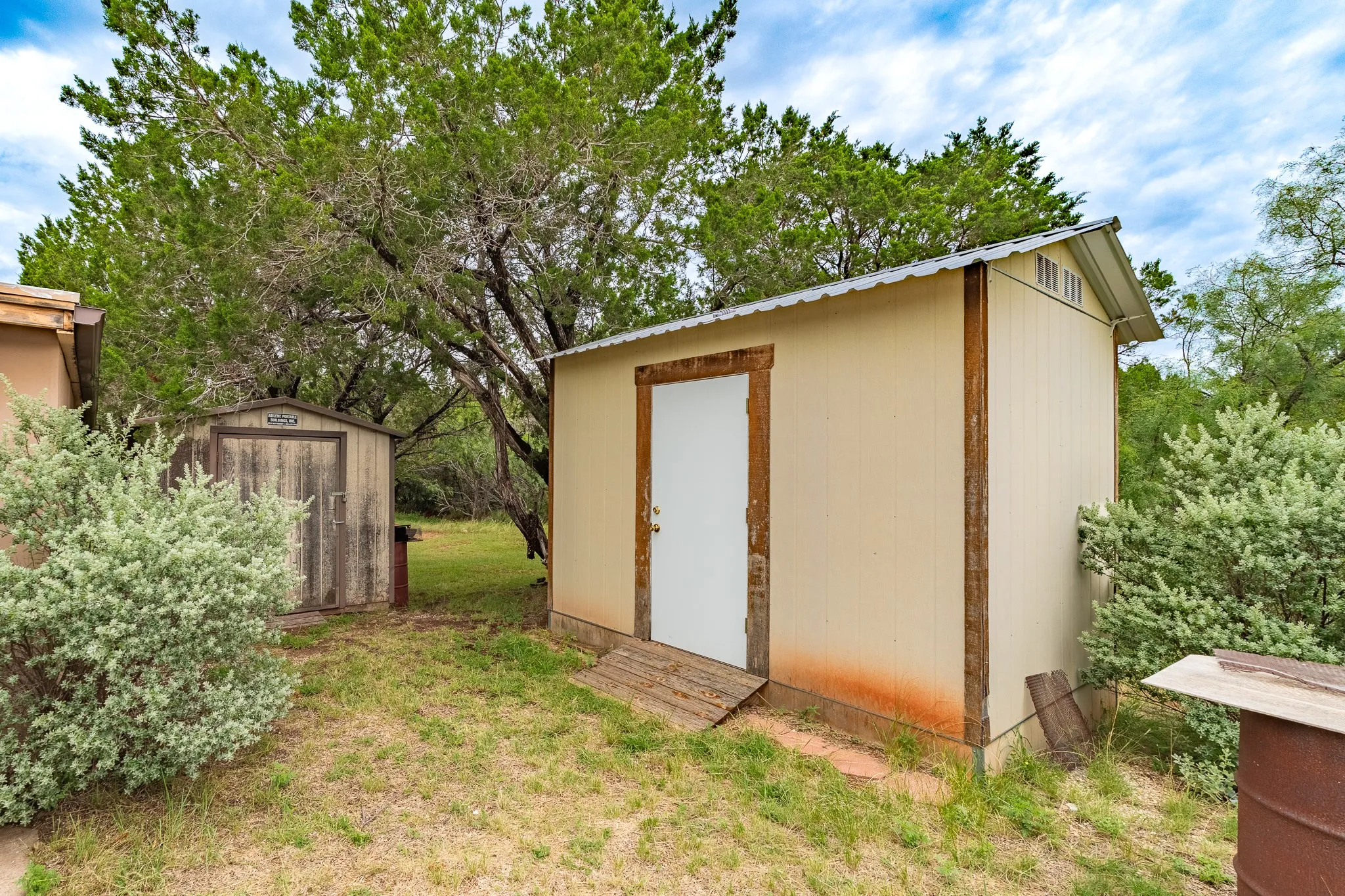 Two outdoor storage sheds featuring wood and metal construction, set amidst natural landscaping