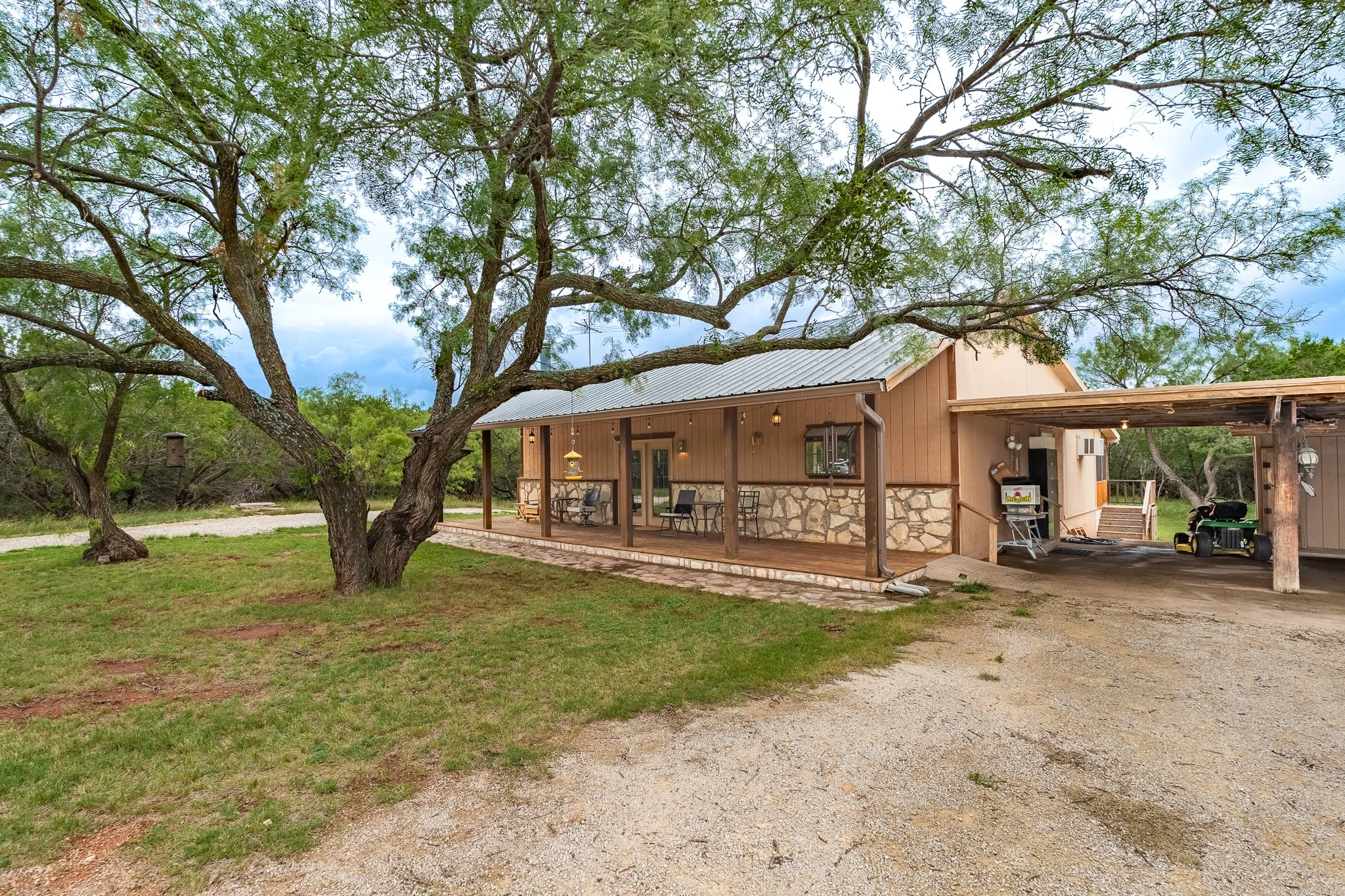 Exterior featuring a full-length covered porch with wood-finish decking, stone wainscoting, and a metal roof