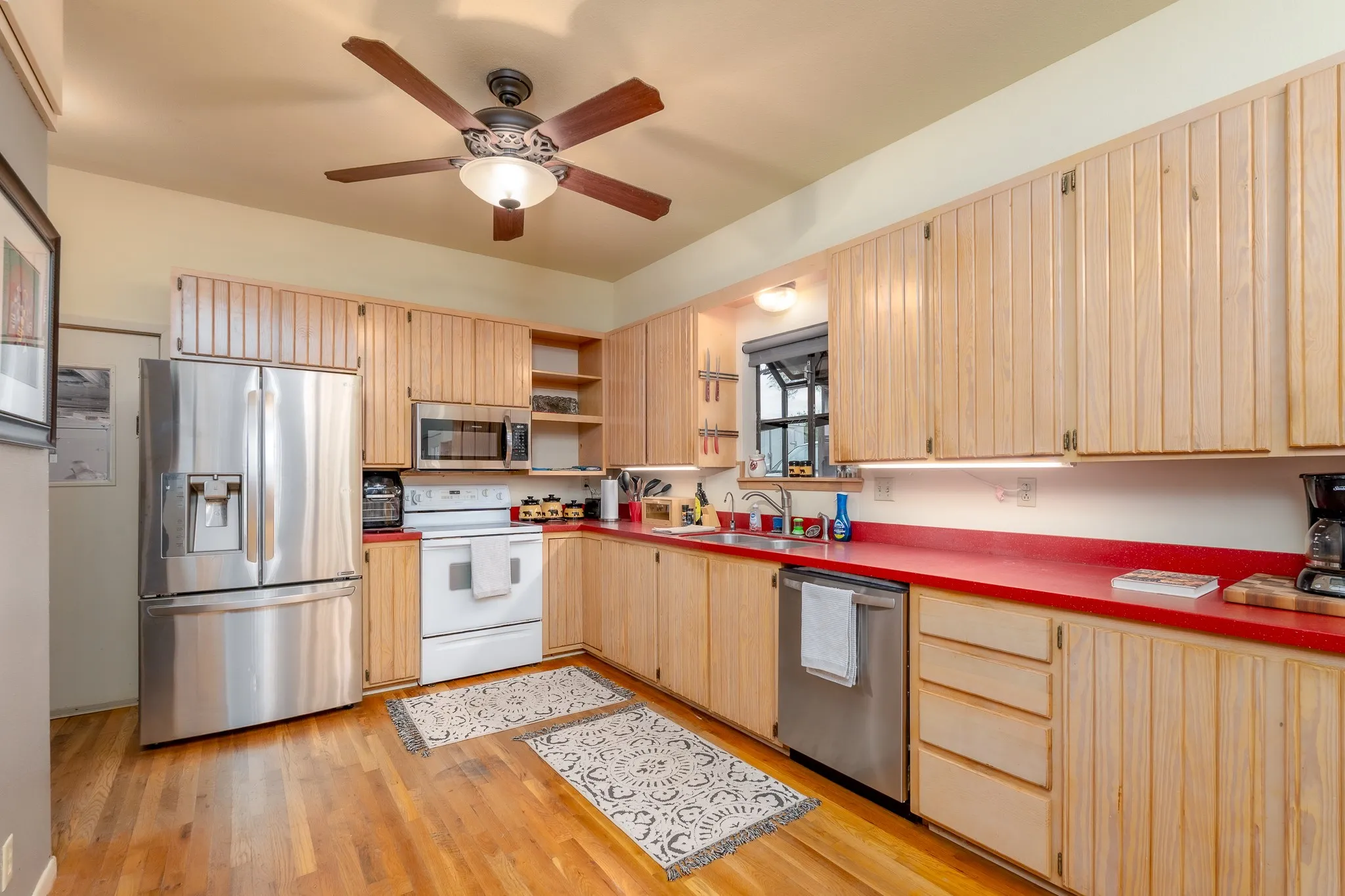 Kitchen featuring wood-finish flooring, natural wood cabinetry, stainless steel appliances, and a ceiling fan with integrated lighting