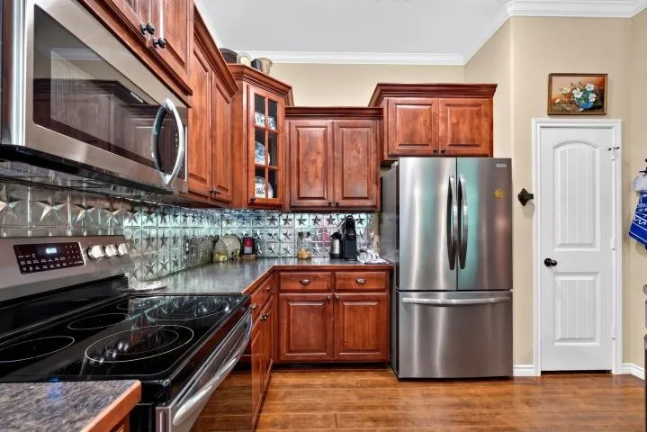 Kitchen featuring stainless steel appliances, wood-finish cabinetry, a textured star pattern backsplash, dark countertops, and wood-finish flooring