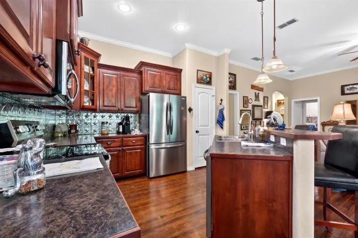 Kitchen featuring wood-finish flooring, dark wood cabinetry, a stainless steel refrigerator, and a patterned backsplash