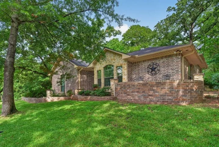 Brick and stone exterior featuring varied architectural elements, mature trees, and a well-maintained lawn