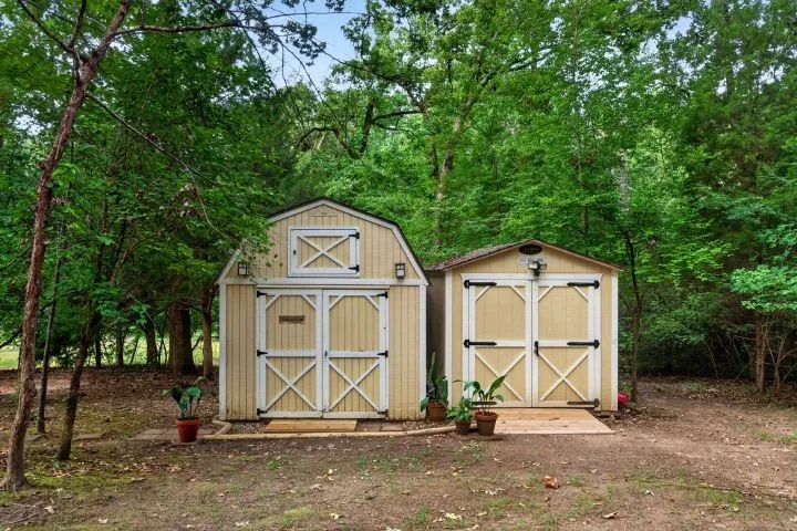Two utility sheds featuring painted wood siding, double barn doors with decorative cross bracing, and black hardware