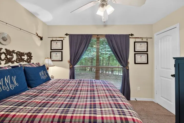 Bedroom featuring light-toned walls, a large window with blinds and drapes, a ceiling fan with integrated lighting, and carpet flooring