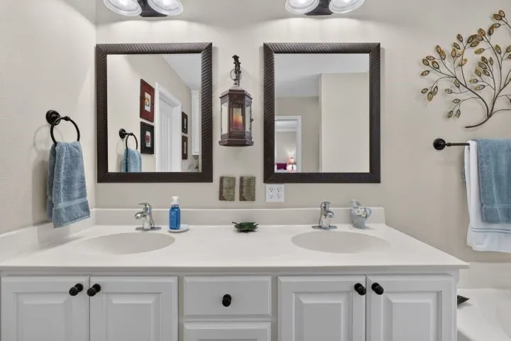 Dual vanity featuring white cabinetry with dark hardware, integrated sinks, chrome faucets, and two framed mirrors