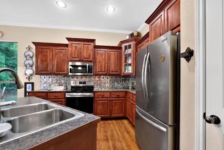 Kitchen featuring cherry wood-finish cabinetry, stainless steel appliances, a double basin sink, and a decorative backsplash