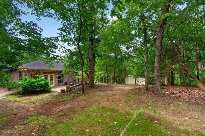 Expansive wooded grounds featuring a brick exterior residence, a rear patio with double doors, and an additional shed structure