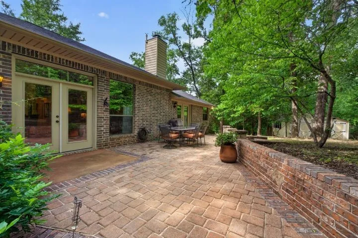 Expansive brick paver patio featuring a brick retaining wall and mature trees
