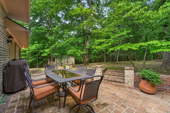 Brick paver patio featuring a partial brick exterior, stone accent columns, and a terraced backyard with mature trees