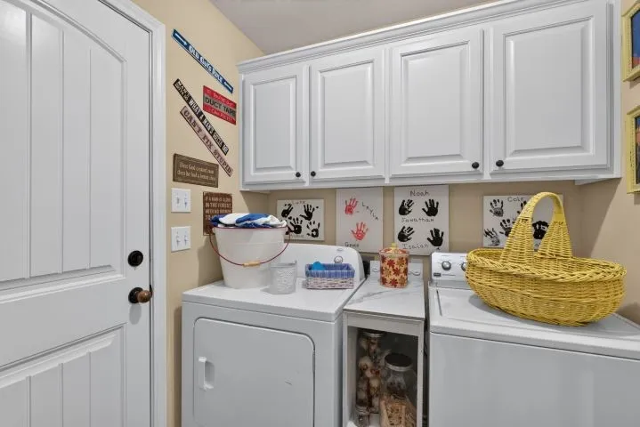 Dedicated laundry area featuring white upper cabinetry with black hardware, a white paneled door with a bronze doorknob, and light-colored walls