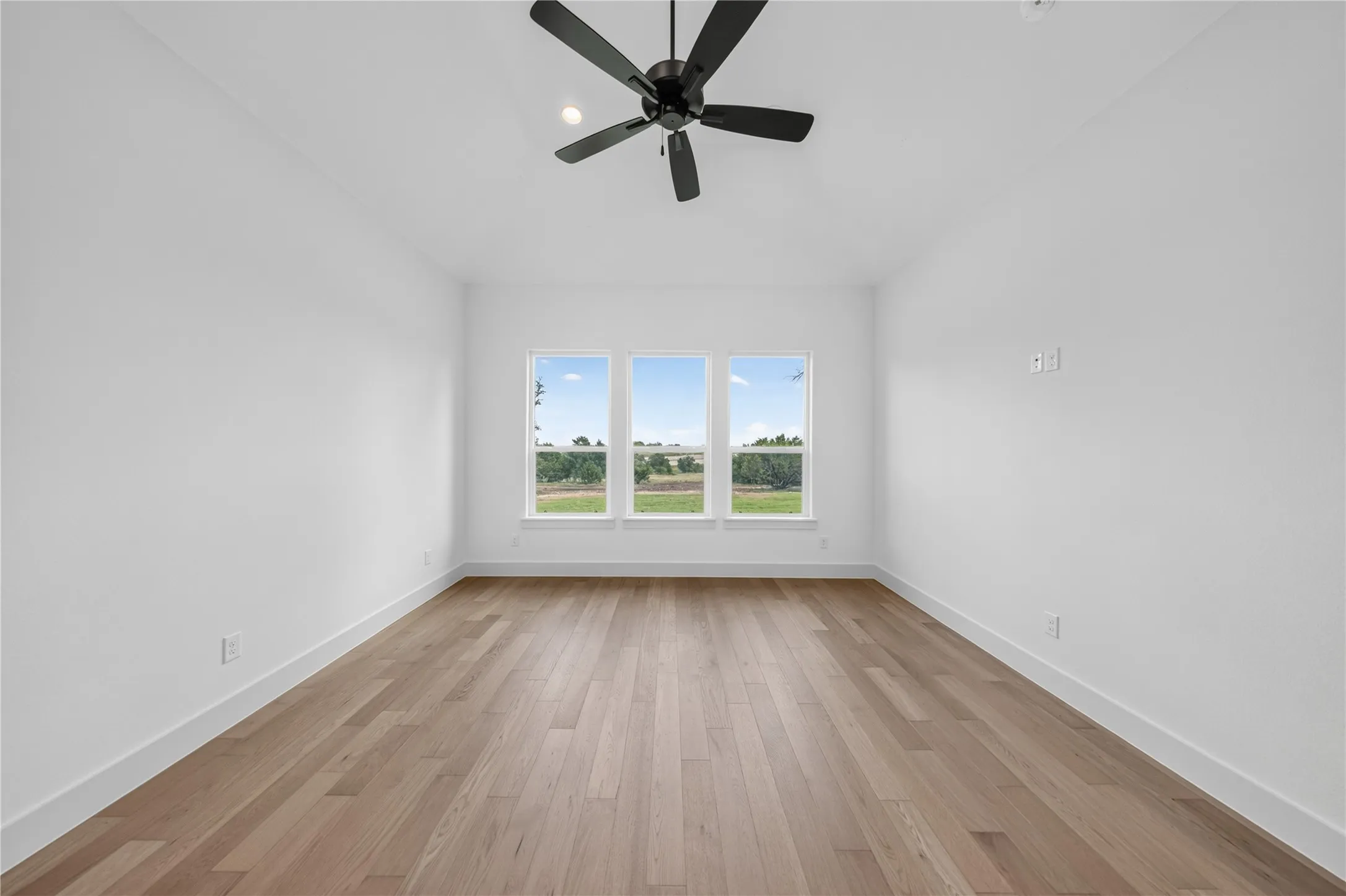 Room featuring wood-finish flooring, white walls, and a matte black ceiling fan