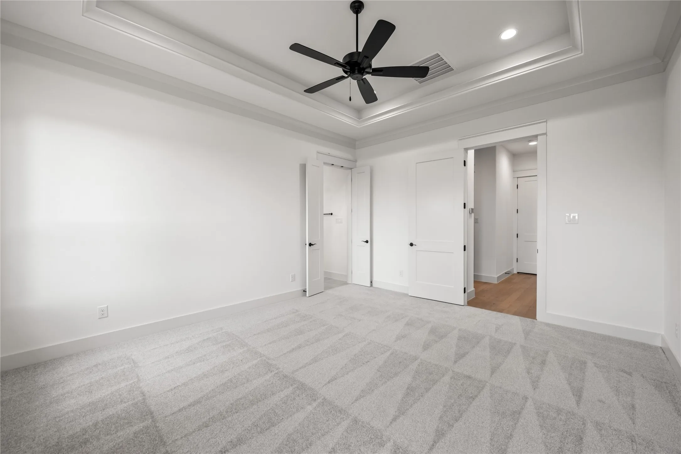 Spacious room featuring a tray ceiling with crown molding and a black ceiling fan