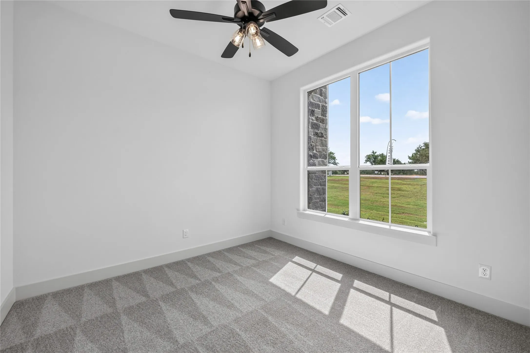 Room featuring a large window, a ceiling fan with integrated lighting, gray patterned carpeting, white walls, and gray baseboards