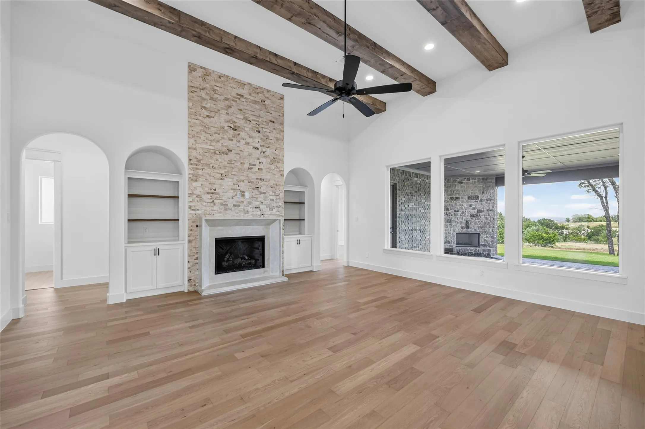 Vaulted ceilings featuring exposed wood beams, a stone-clad fireplace with a hearth, and built-in arched shelving