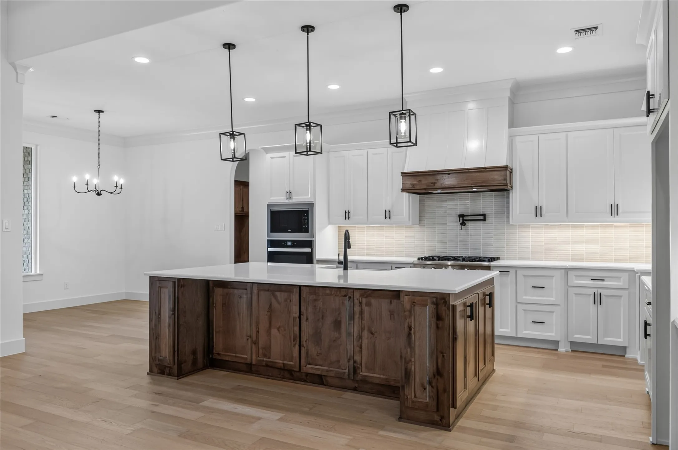 Spacious kitchen featuring a large wood-finish island with a light-toned countertop, white cabinetry with dark hardware, a tile backsplash, and wood-finish flooring