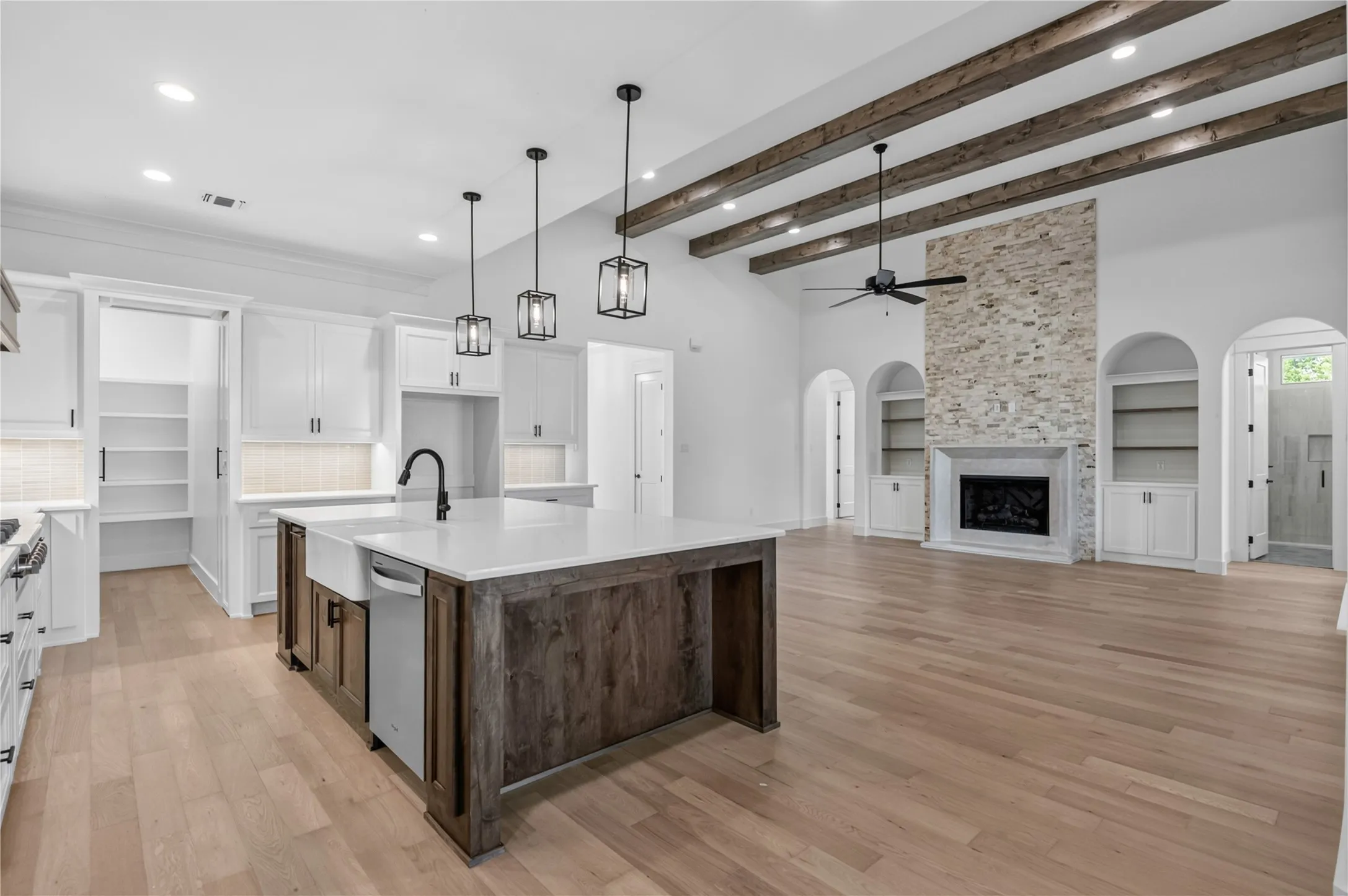 Spacious kitchen and living area featuring a large center island with a farmhouse sink, white cabinetry, and wood-finish flooring