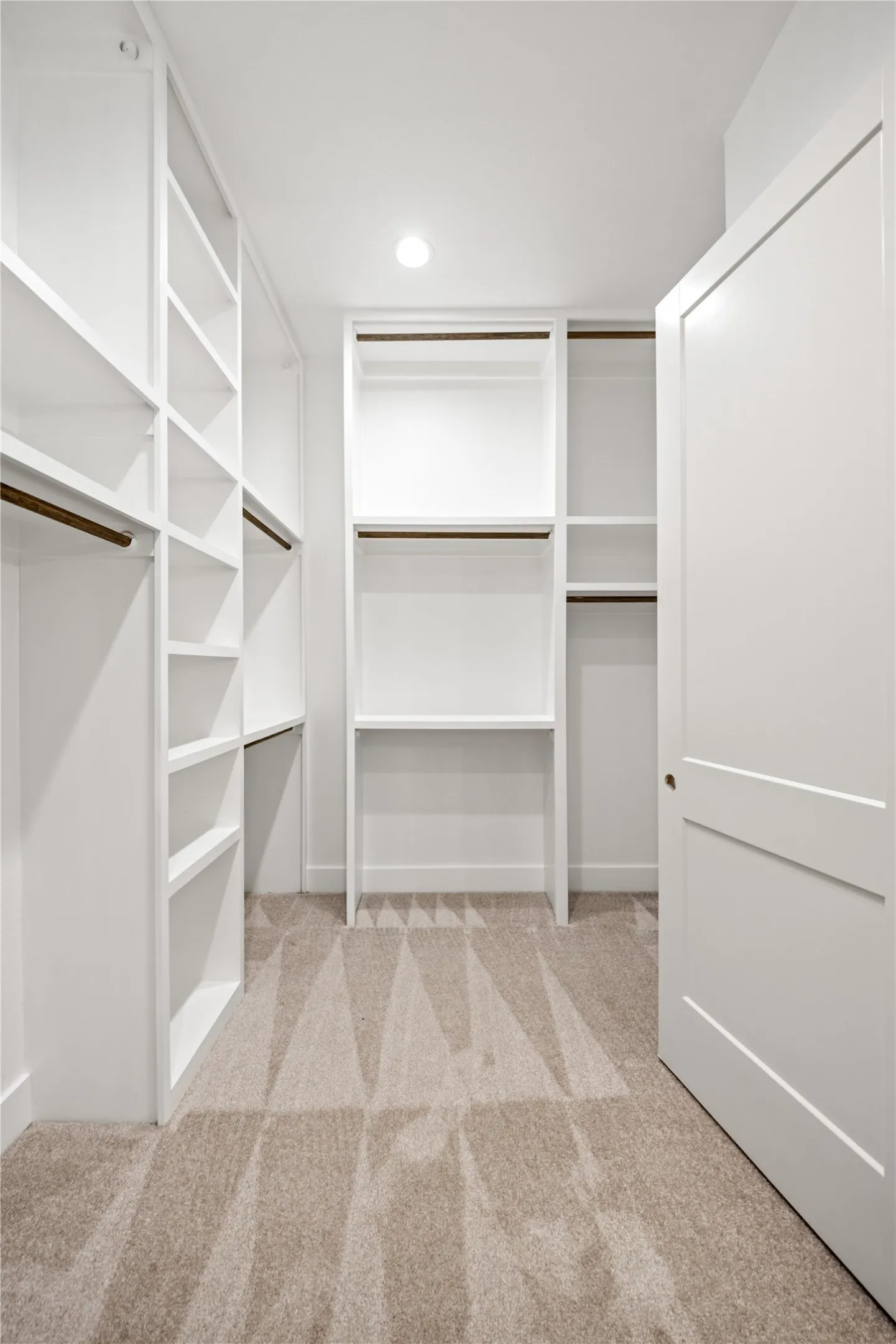 Walk-in closet featuring built-in shelving, integrated hanging rods, recessed lighting, and neutral-toned carpet flooring