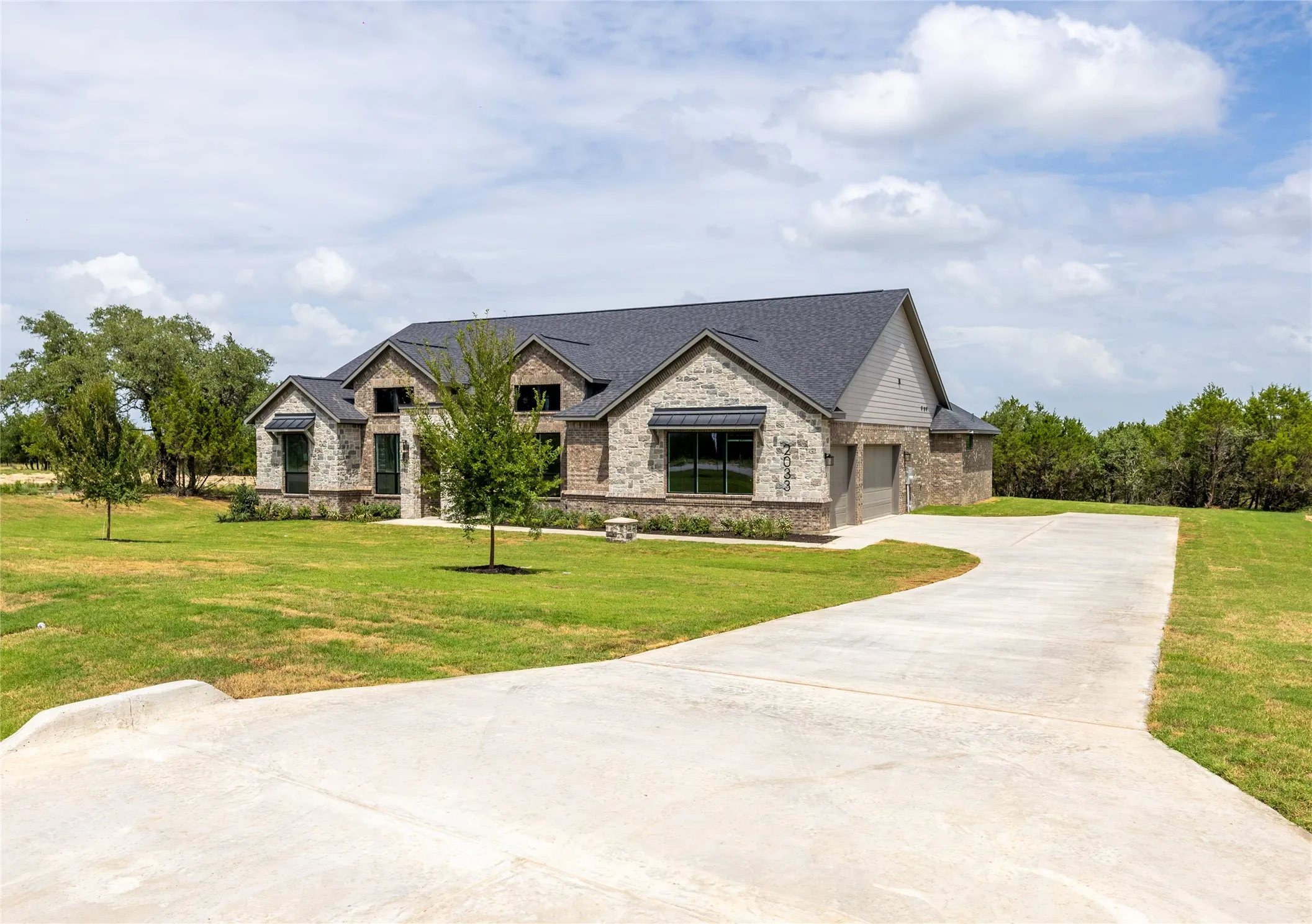 Stone and brick facade home featuring a dark shingle roof and a grey siding gable