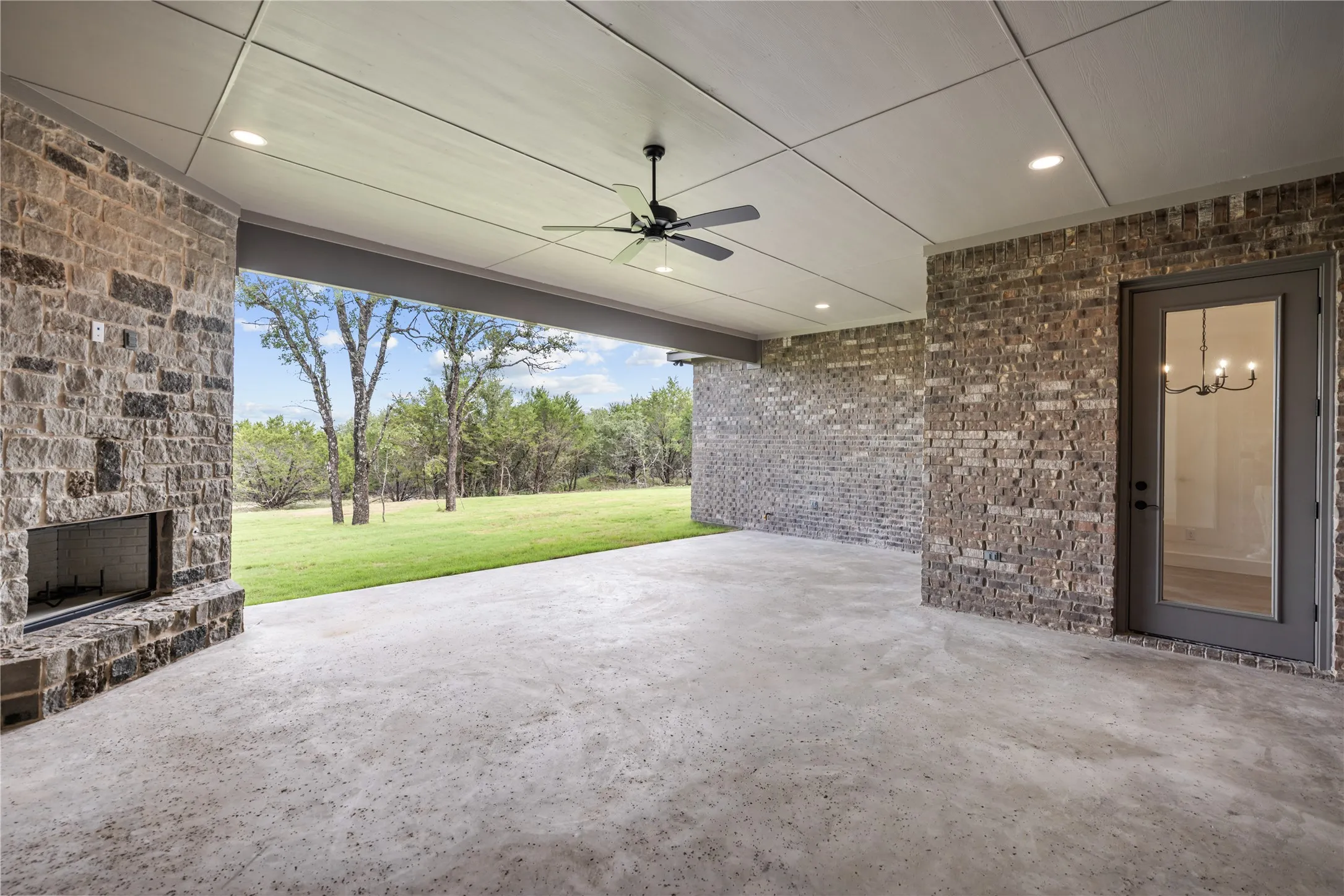 Expansive covered patio featuring a stone fireplace, brick exterior walls, and a concrete slab