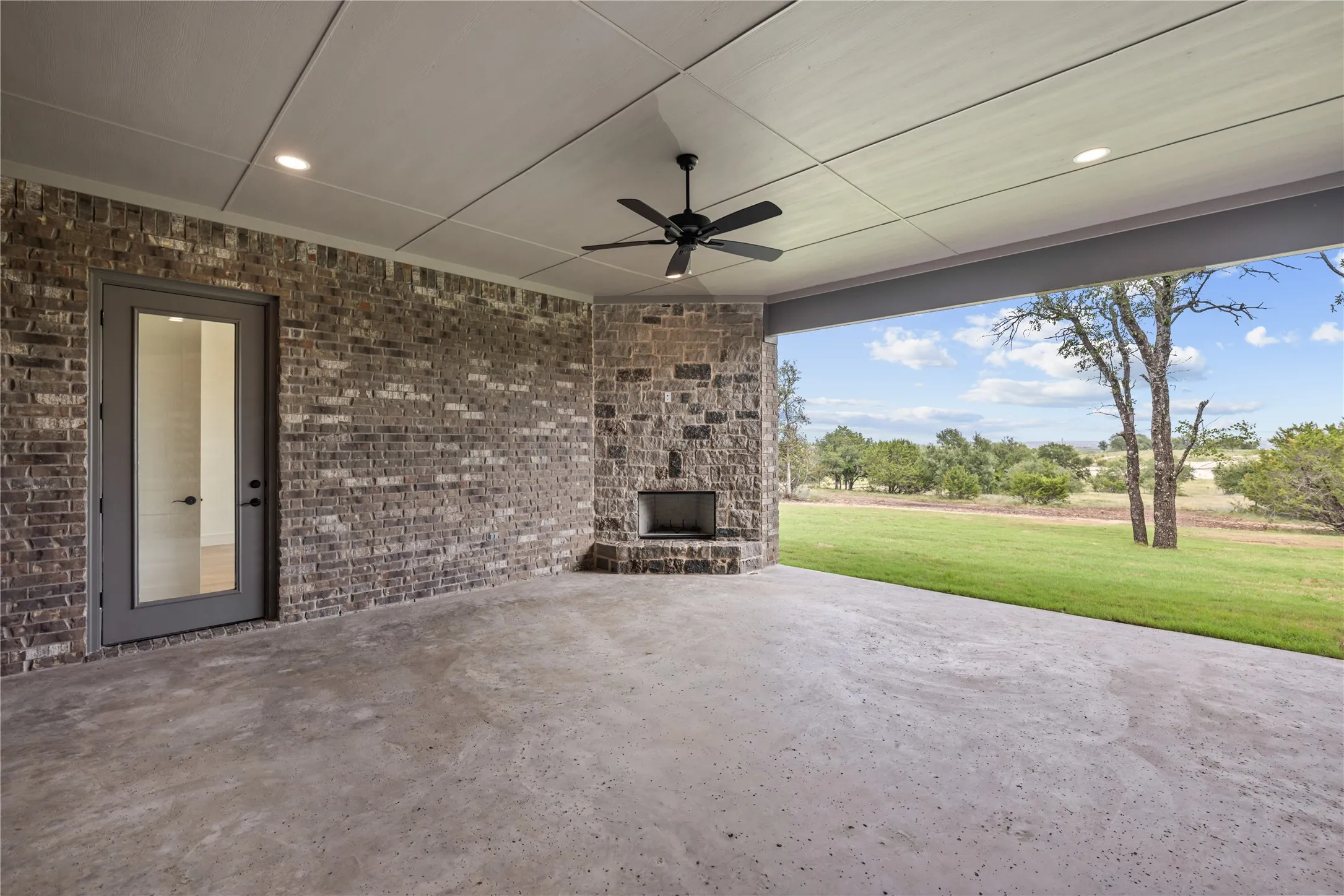 Covered patio featuring a brick exterior and stone fireplace