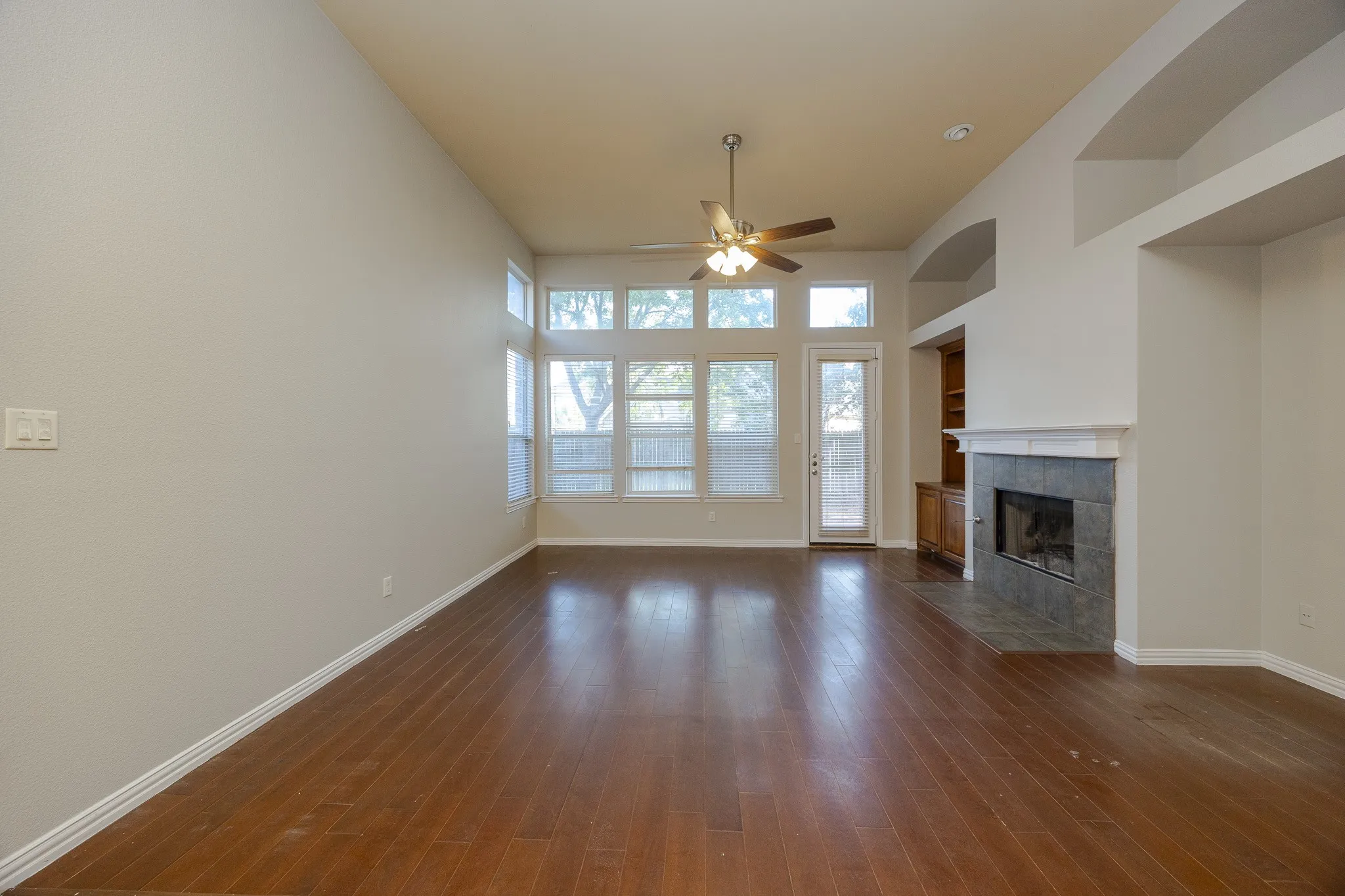 Vaulted ceiling, wood-finish flooring, fireplace with tile surround and mantel, built-in cabinetry, and multiple windows