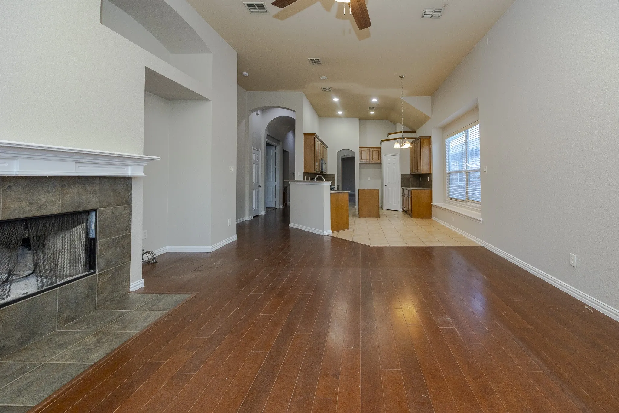 Spacious living area featuring wood-finish flooring, a tiled fireplace, and a high vaulted ceiling