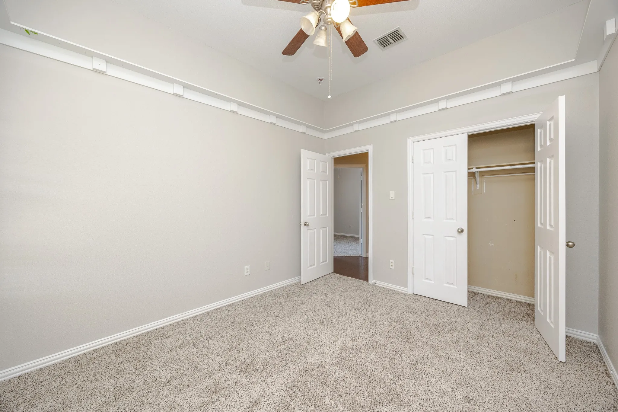 Tray ceiling with crown molding, ceiling fan, neutral wall paint, carpet flooring, and bi-fold closet doors