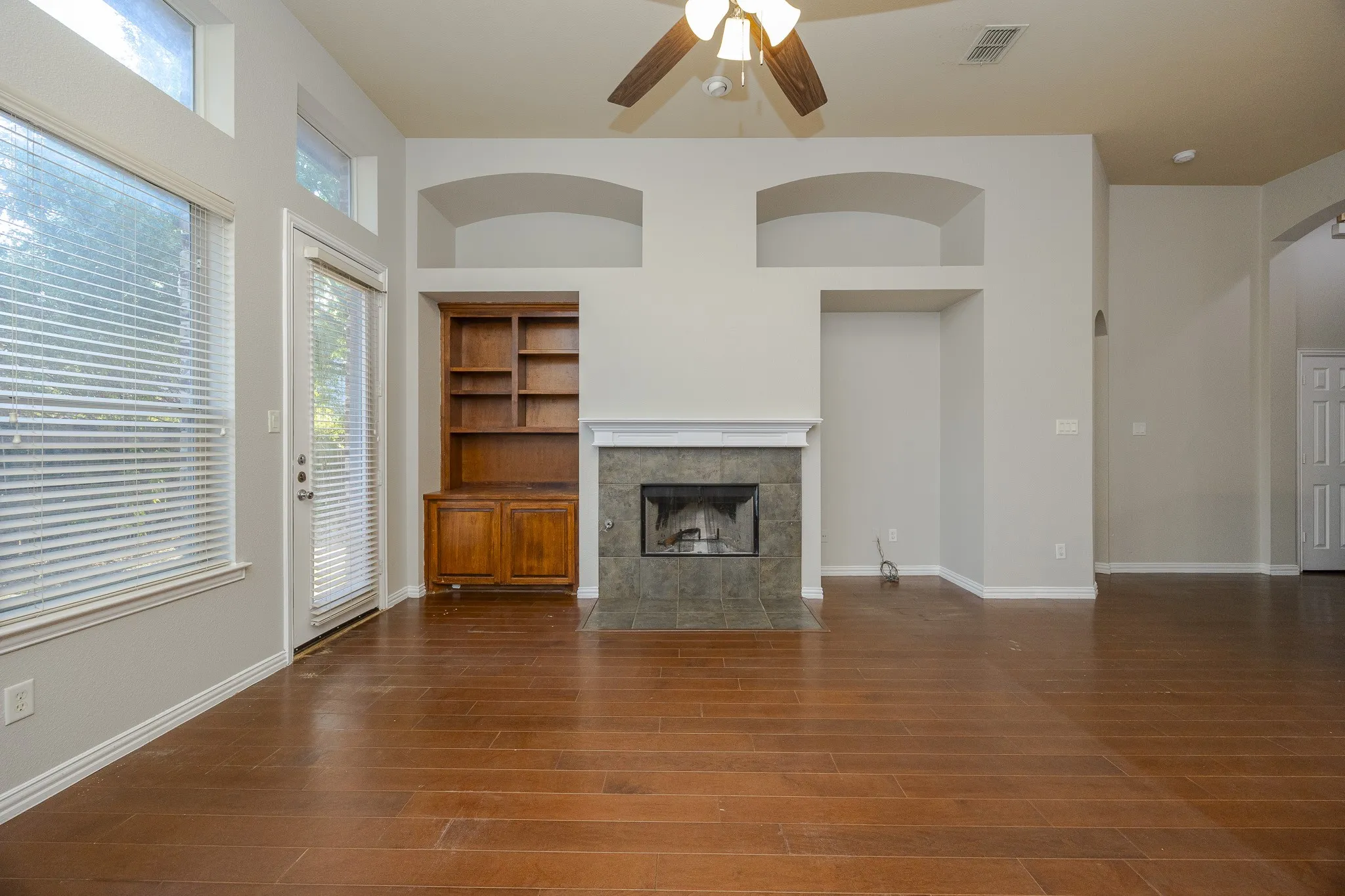 Hardwood-finish flooring, built-in shelving, stone-tiled fireplace, ceiling fan, and transom windows