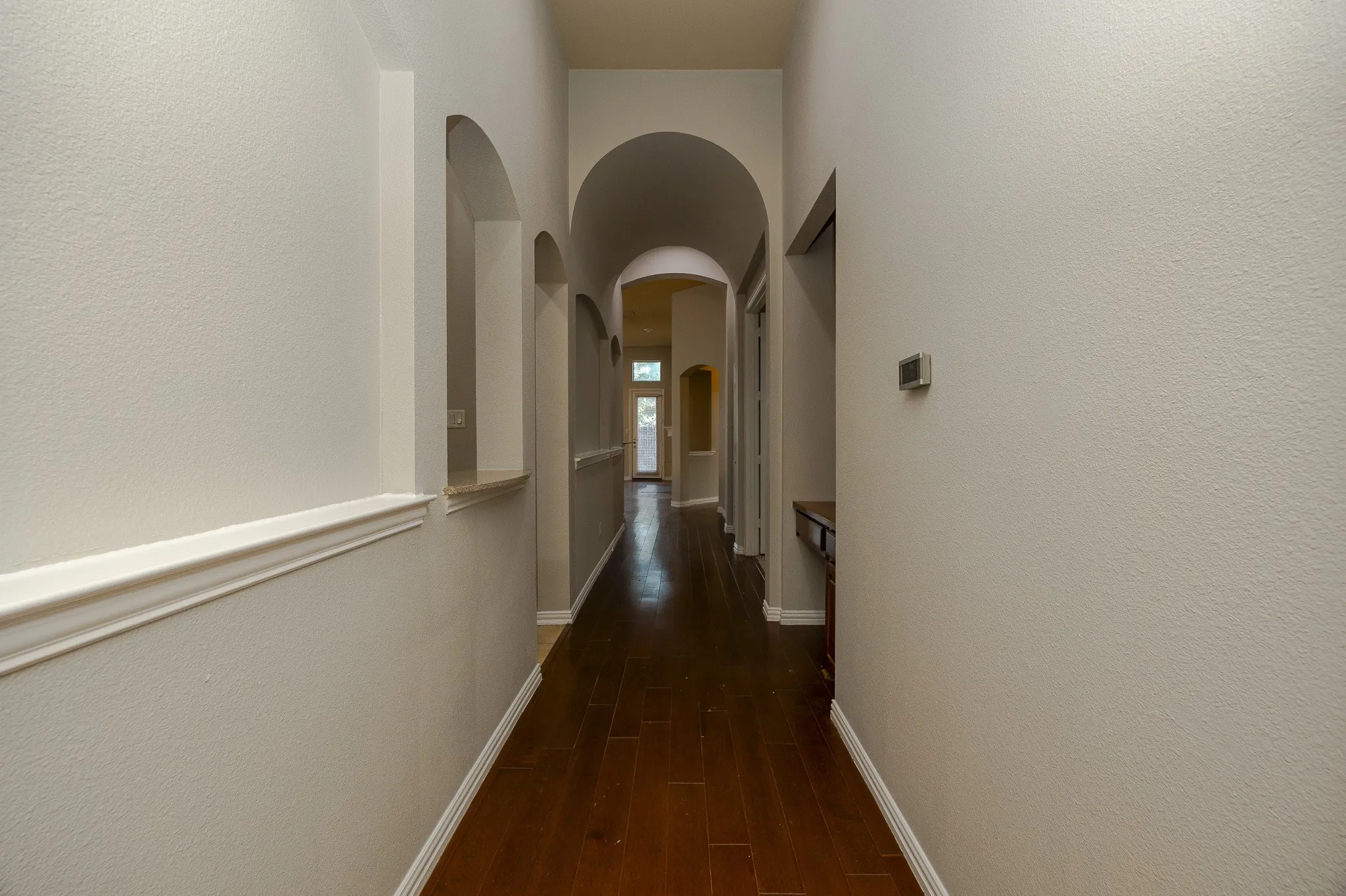 Hallway featuring wood-finish flooring, arched doorways, and light-toned wall finishes