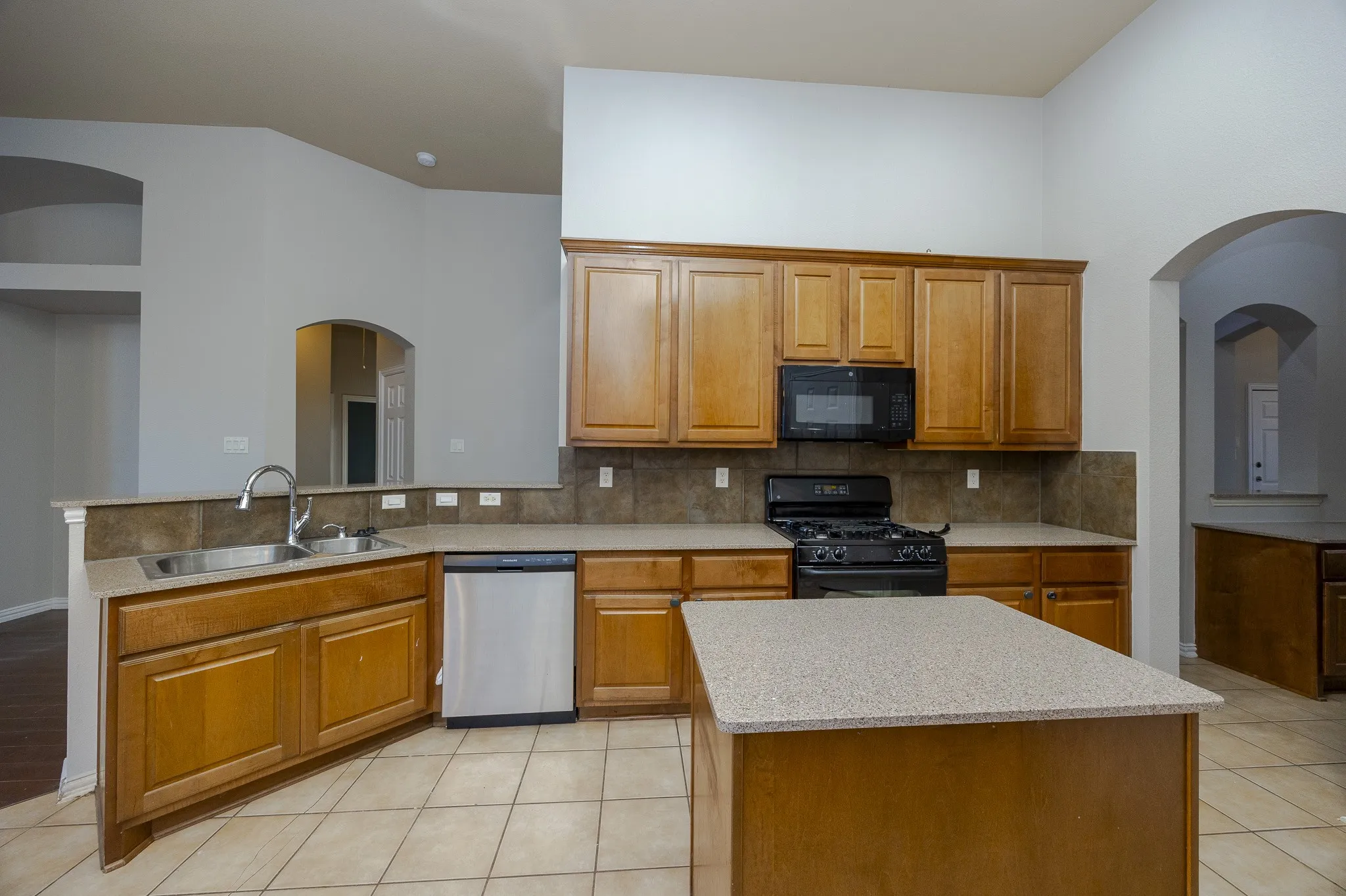 Kitchen featuring a central island, tile flooring, stainless steel dishwasher, and arched architectural details