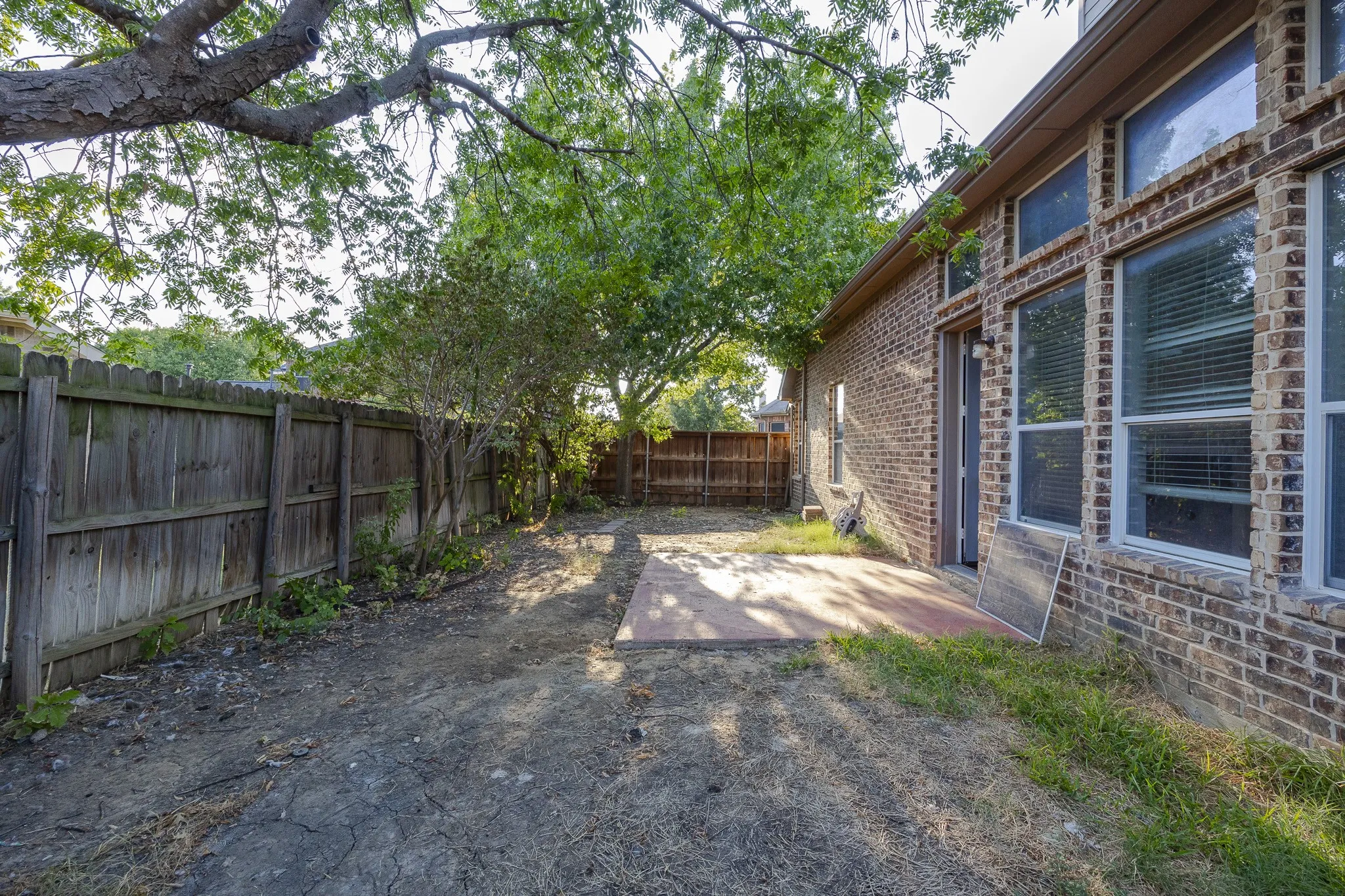 Brick exterior with multiple windows, mature trees, and a wooden privacy fence