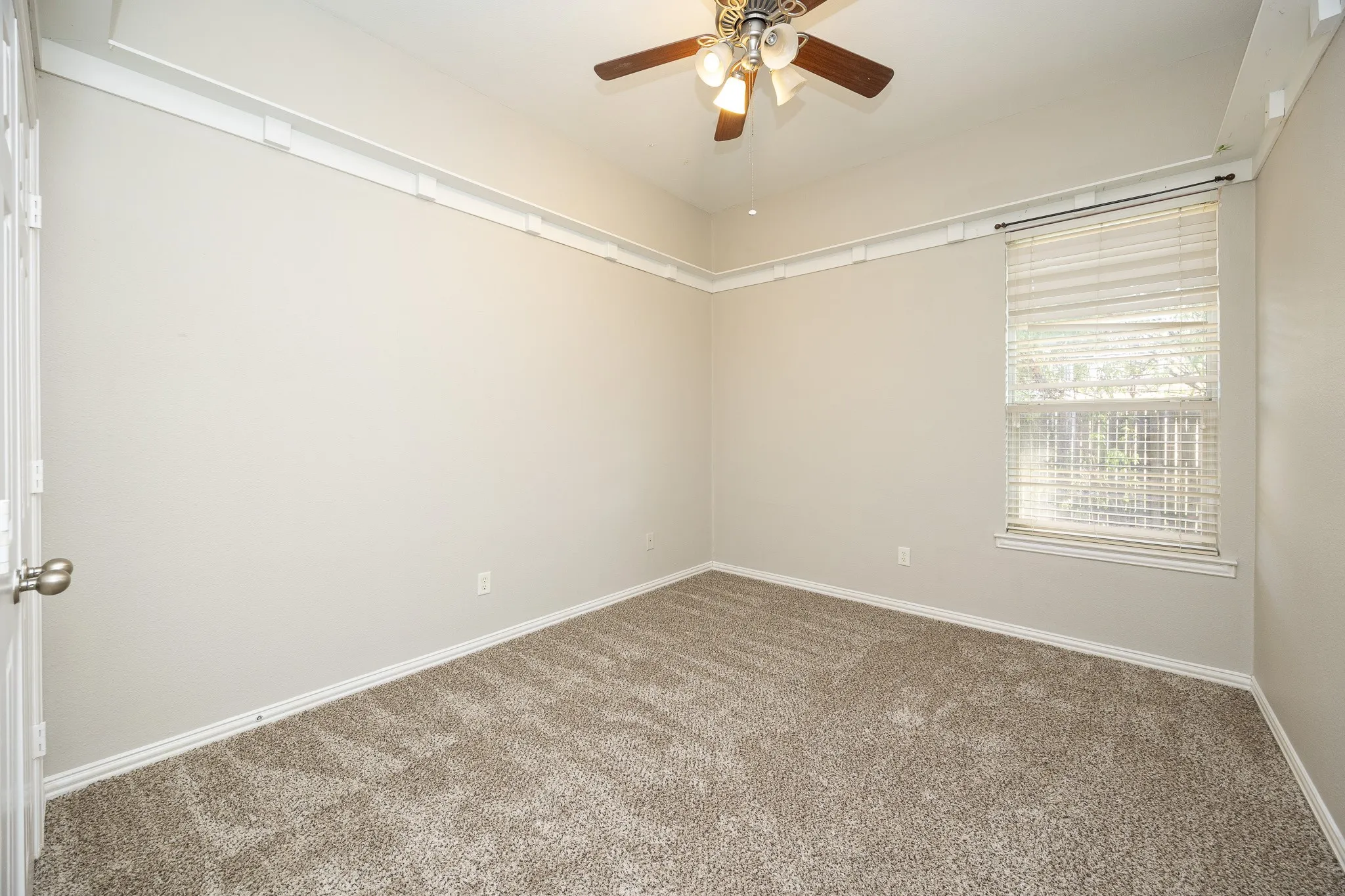 Neutral tone wall paint, carpeted flooring, window with blinds, ceiling fan with light fixture, and crown molding detailing