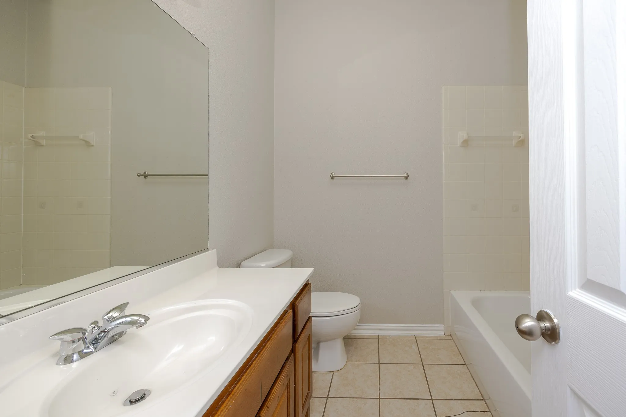 Bathroom featuring a single vanity with wood-finish cabinetry, a white countertop with an integrated sink, a large wall mirror, and a white bathtub with a tiled surround