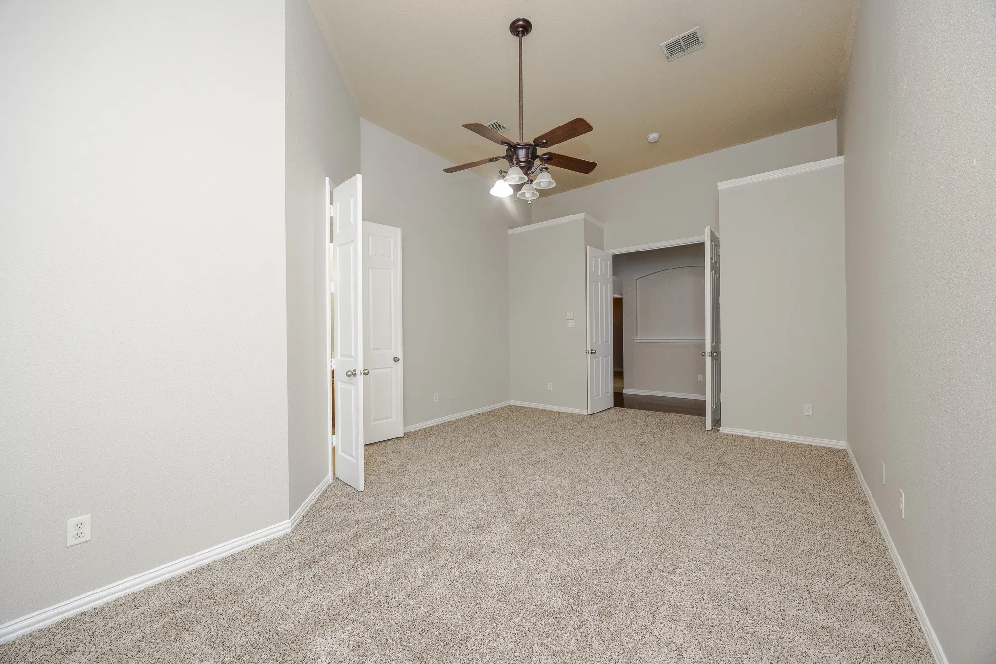 Spacious bedroom with neutral carpet flooring, ceiling fan with integrated lighting, and white six-panel closet doors