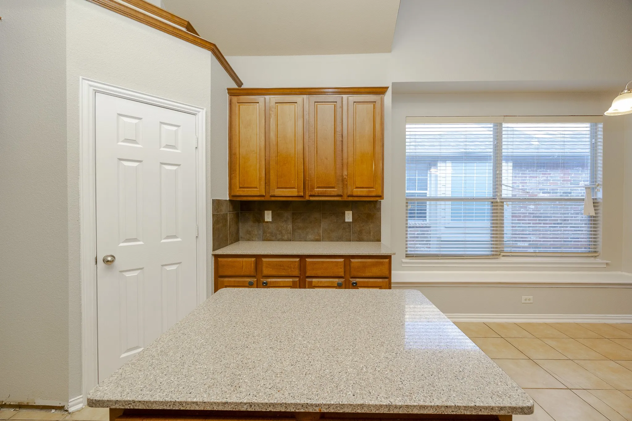 Kitchen island with a speckled countertop, wood cabinetry, tile backsplash, and tile flooring
