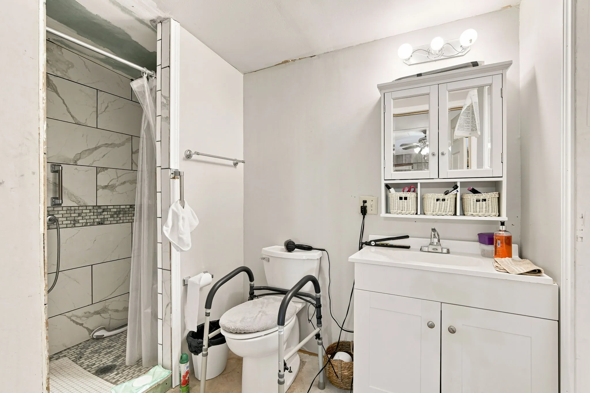 Bathroom featuring a shower with large format tile and a mosaic accent band, a white vanity with an integrated sink, a wall-mounted medicine cabinet with mirror doors, and a three-bulb vanity light fixture
